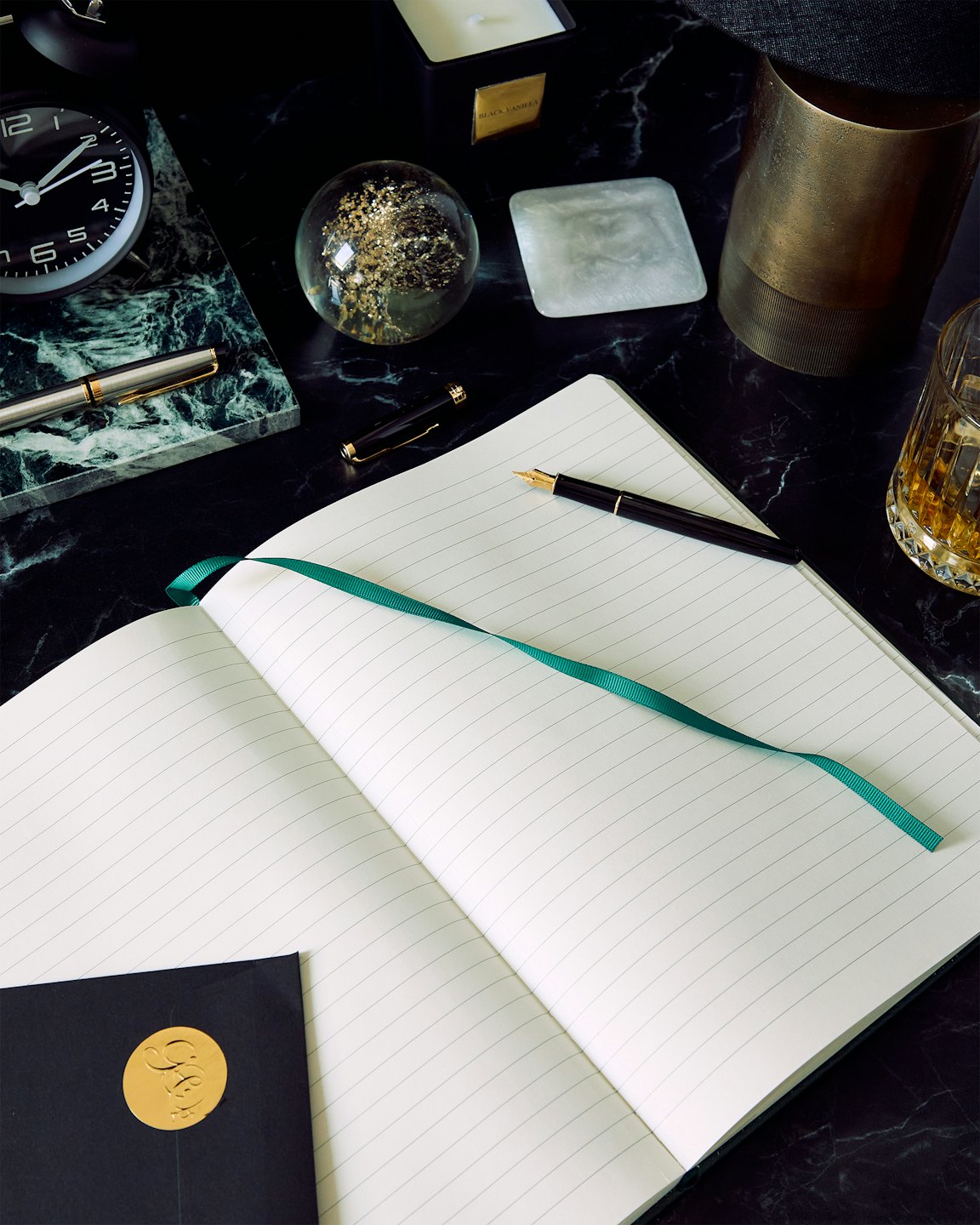 Notebook and pens arranged on a dark marble desk surface.