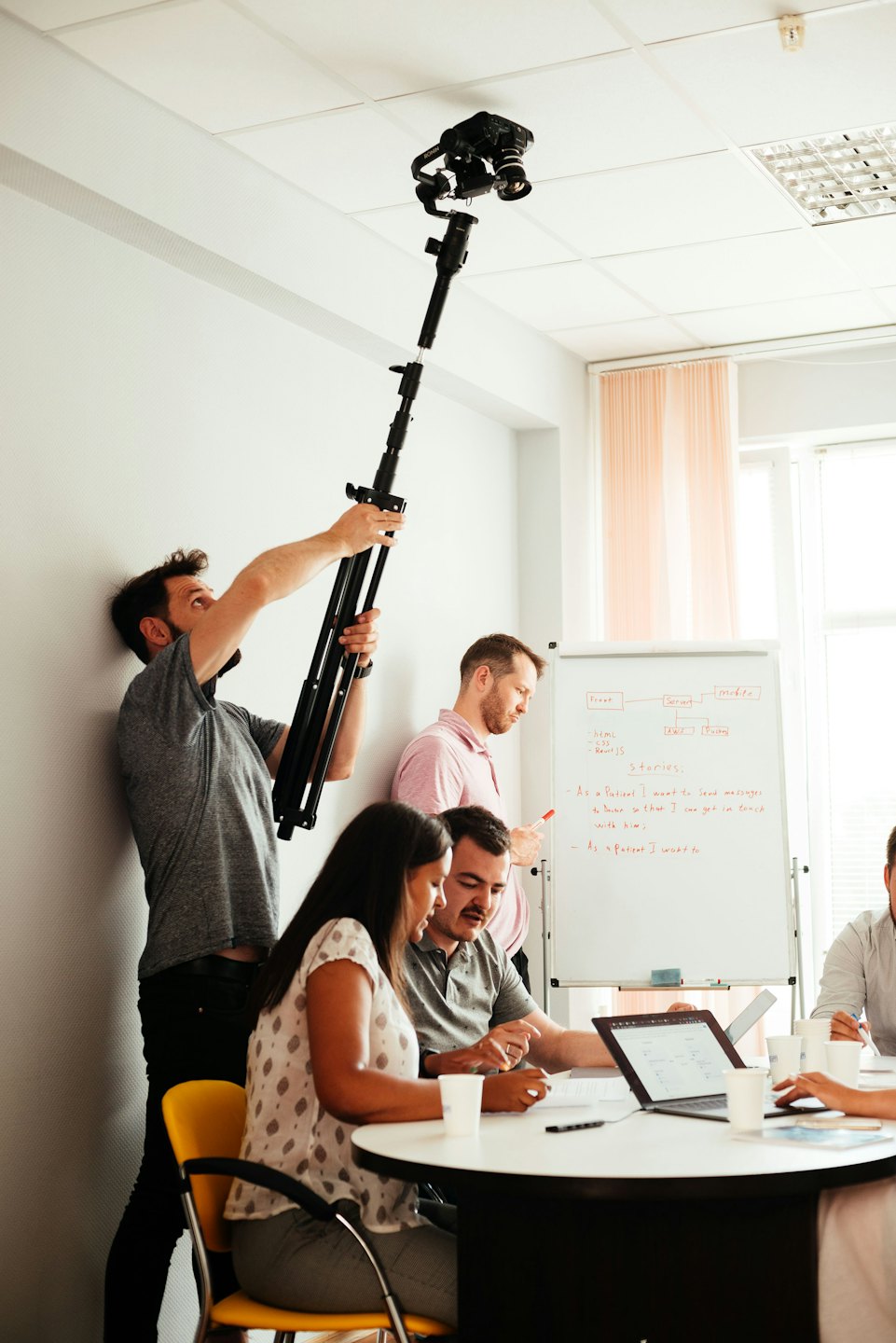 Professionals collaborate in an office with a man adjusting a camera on a pole.