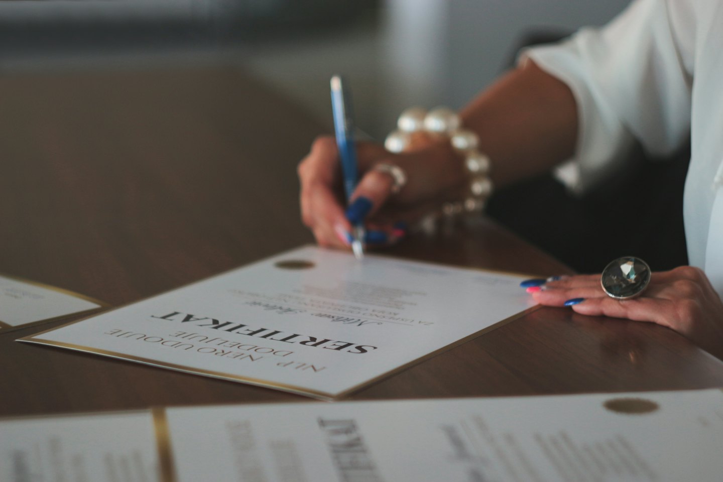 Hands signing a certificate with a blue pen on a wooden table.